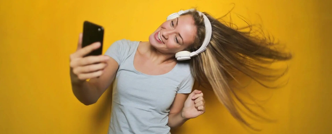 A woman wearing headphones looking at her smartphone and smiling