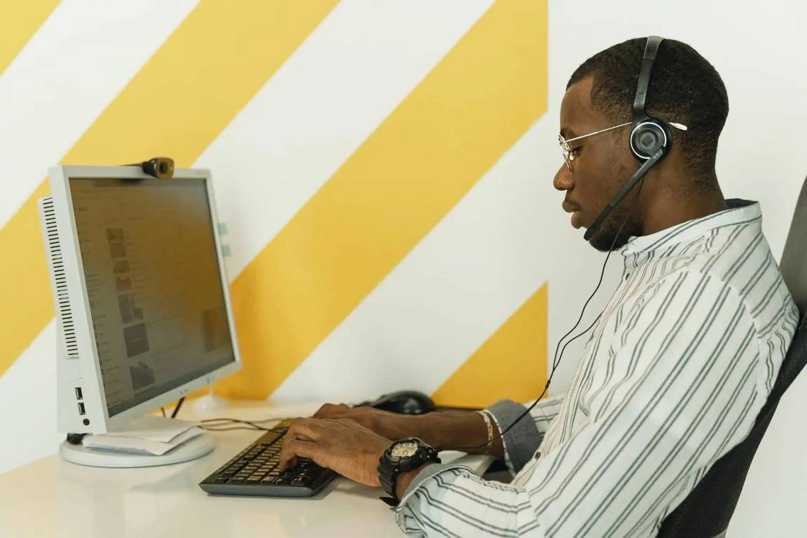 A man wearing a headset sitting at his desk and working on his computer.