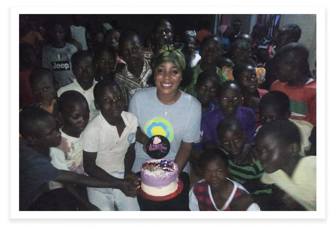 Adesuwa Ogbemudia smiles in the center of a group of children, holding a cake.