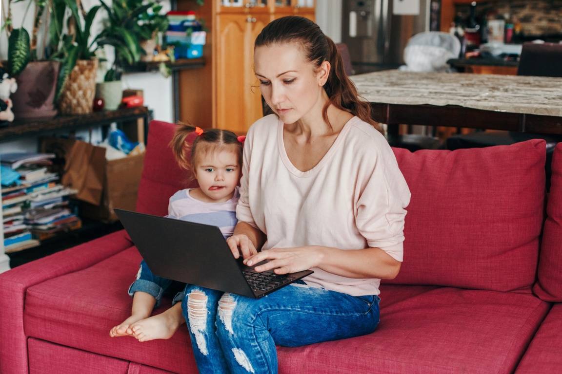 A woman working on her laptop on the couch next to her daughter.