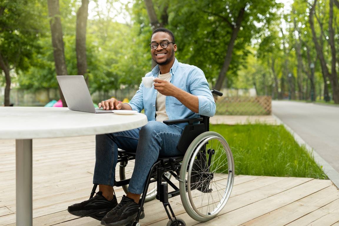 A smiling black man in a wheelchair looks forward holding a tea cup.