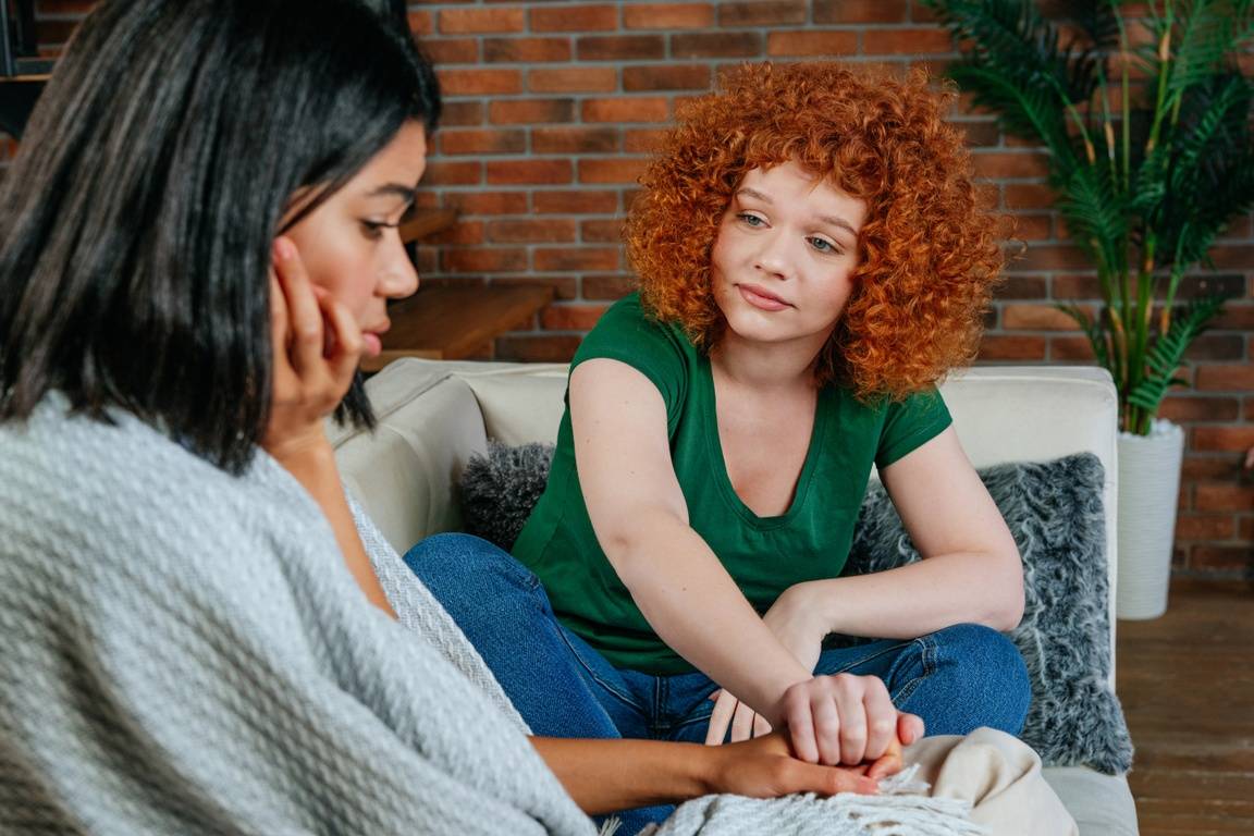 One woman holds the other's hand to comfort her.
