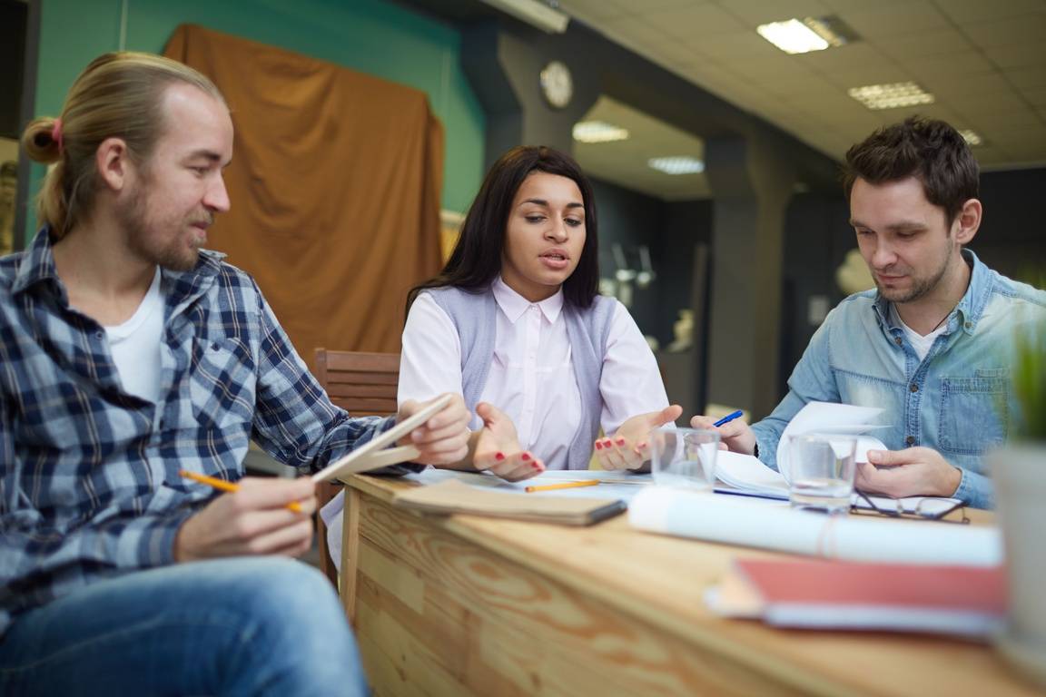 Two men and a woman sit around a table with pens and paper discussing a new project.