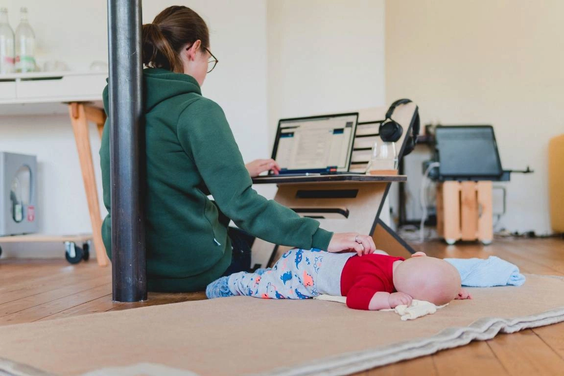 A woman working remotely while caring for her child
