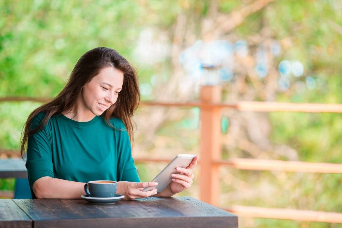 A woman happily looks at her smart phone while sitting alone in coffee shop during free time.