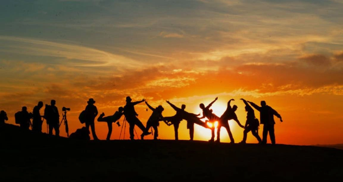 A group of people on a mountain posing and looking at the sunset.