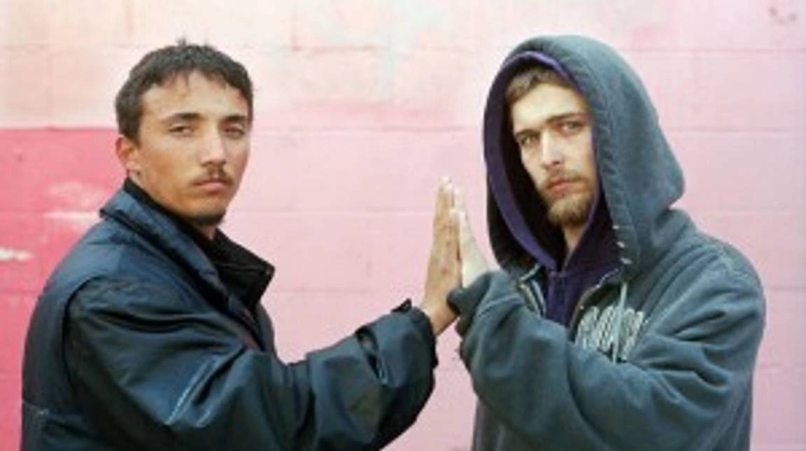 Two men with their hands together, in a high five, looking at the camera.