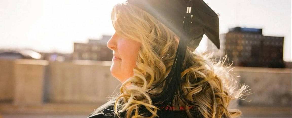 Profile-view image of a woman wearing a graduation cap looking into the sunlight