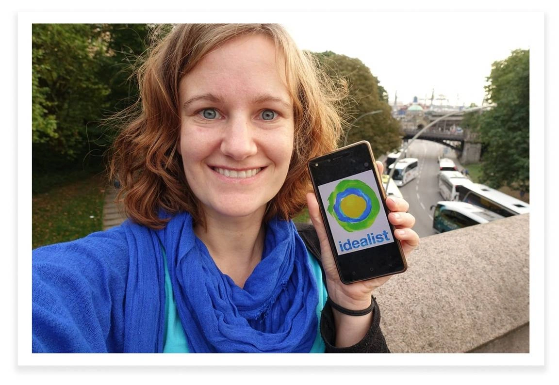 Susanne Friedrich, founder of Green Spark holding up a phone with the Idealist logo on it.