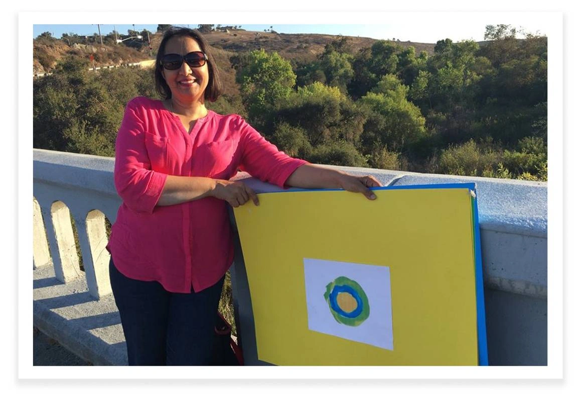 Mehreen Hussein, an idealist from California poses next to the Idealist logo in front of a balcony.
