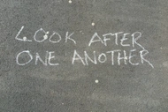 "Look after one another" written in chalk on concrete.
