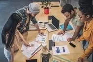 A photograph of different team members looking over project plans at a long table in the office.