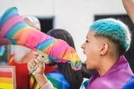 A photograph of a young person with short, blue-dyed hair yelling into a megaphone at an LGBTQ+ pride demonstration.