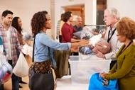 A photograph of a Black woman donating a bag of clothes at a clothing donation drive.
