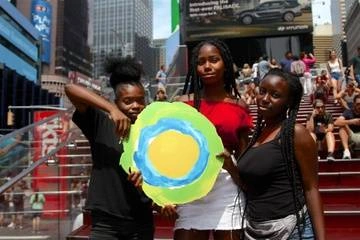 Three children hold up the Idealist logo on the stairs in Times Square.