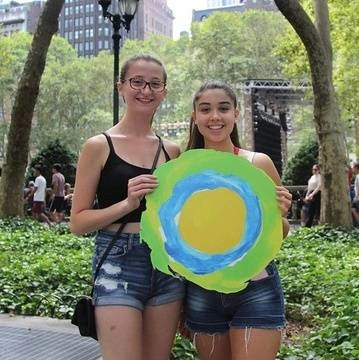 Two young ladies pose in the park with the Idealist logo.