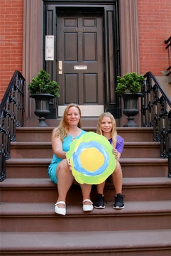 Two people sitting on a stoop with the Idealist logo between them.