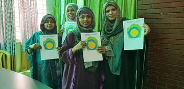 A group of women with head coverings hold up papers with the Idealist logo on it.