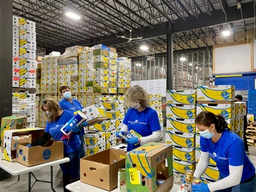 Volunteers at Good Shepherd Food Bank of Maine in front of a wall of banana boxes in the Auburn Distribution Center.