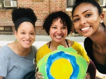 Three women smiling with the Idealist logo between them.
