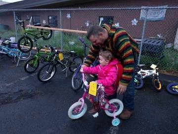 A dad helps his little girl test ride a bike at the Kids Swap