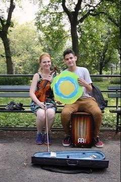 Two people sit next to each other in the park holding the Idealist logo.