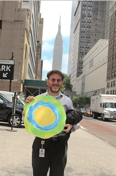 A man holding the Idealist logo poses in the street.