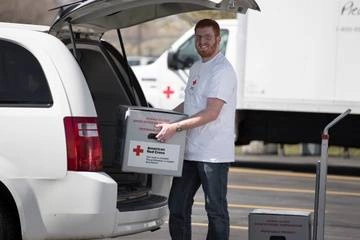 Man loading blood transportation container into Red Cross van