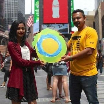 Two people in Times Square pose with the Idealist logo between them.