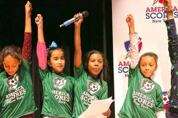 four young female students with fists raised in the air onstage at a NYC youth poetry slam