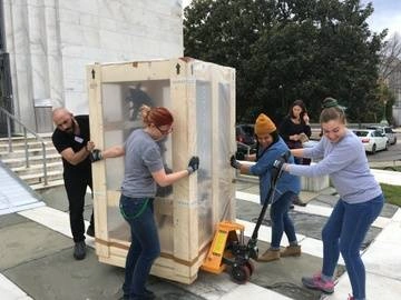 5 Folger staff working together to bring out exhibits; hauling a large exhibit object outside in front of Folger steps prepping for renovation