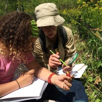 Adult and student outdoors recording nature in notebooks