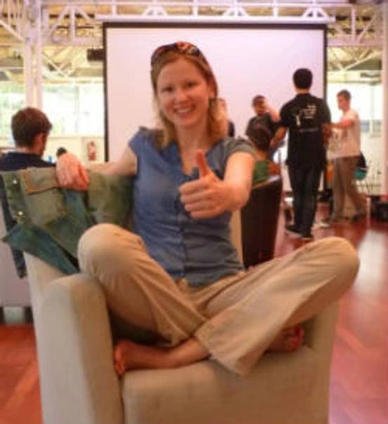 Woman sitting cross legged on a chair with a two thumbs up.