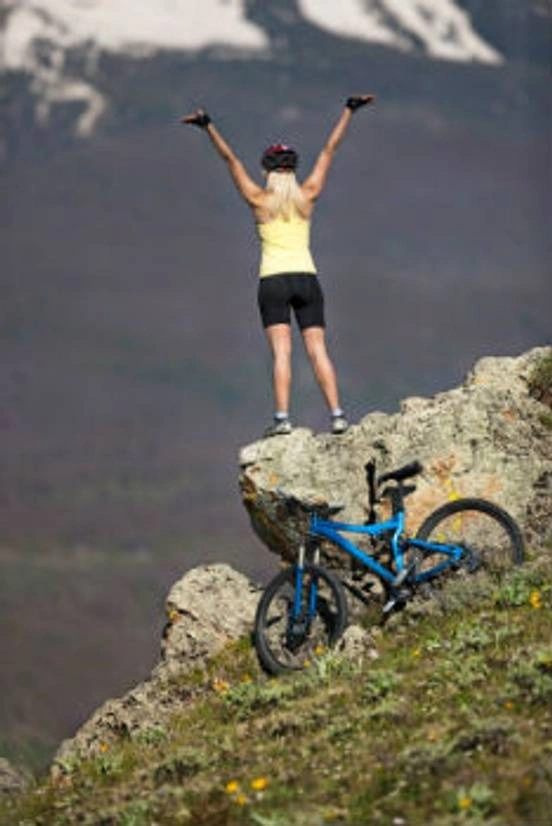 Woman standing victoriously on top of a mountain with her bike nearby