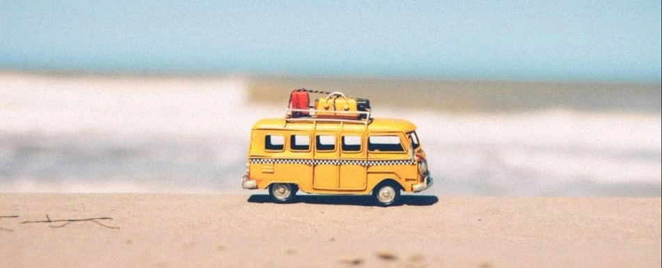 A miniature yellow van with suitcases on top.