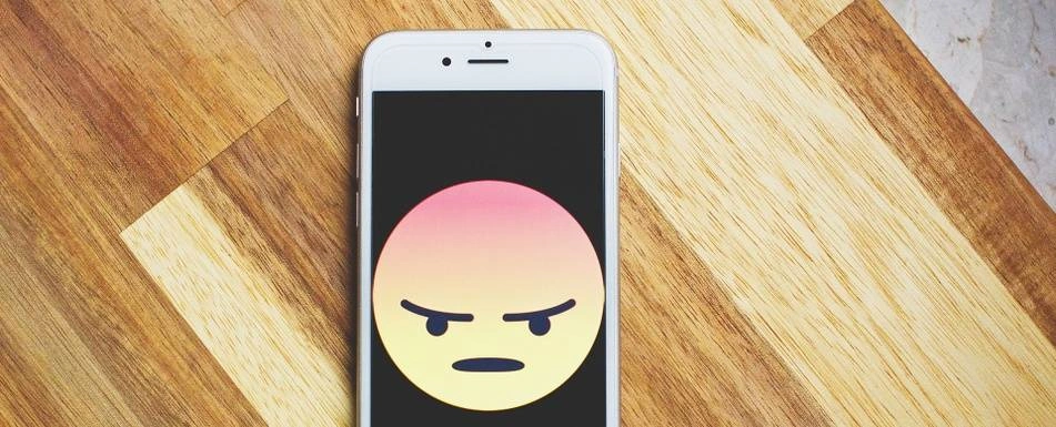 A smartphone with an angry face emoji on  the screen.