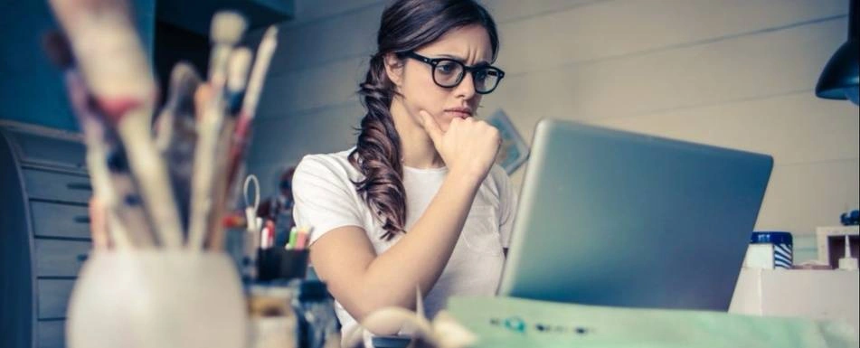 A woman looks at her laptop with her hand on her chin.