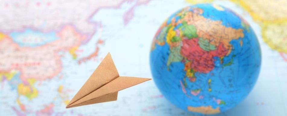 A picture of a globe with a paper airplane next to it.