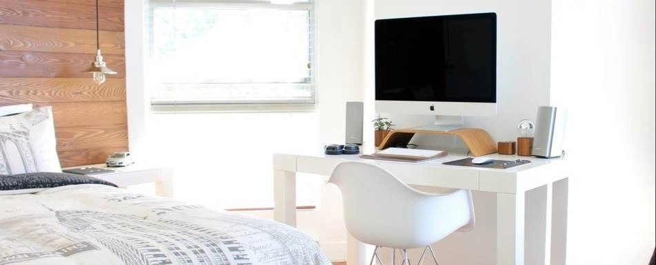 A bedroom with a bed and a work desk with headphones, an iMac and speakers.
