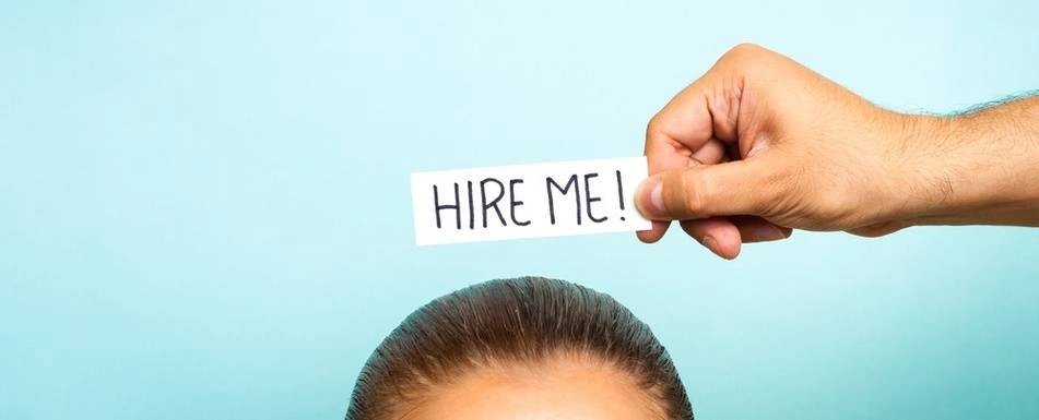 Someone holding a sign that says 'Hire Me' on top of someone's head.