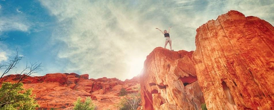 A person standing on a cliff with their hands up in the air.