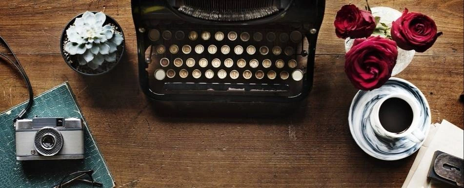 A typewriter on a desk. There is also a mug and a vintage camera.