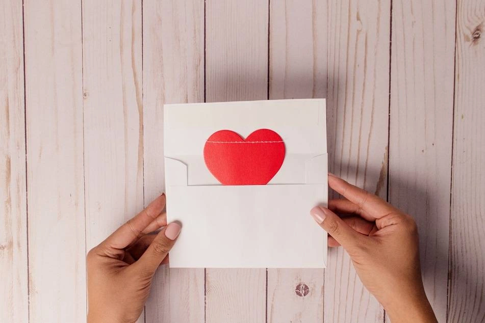 Una mujer saca una postal con un corazón rojo de un sobre
