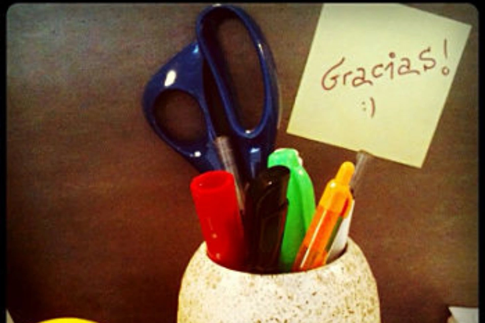 Una nota de Gracias junto a un vaso con materiales de oficina