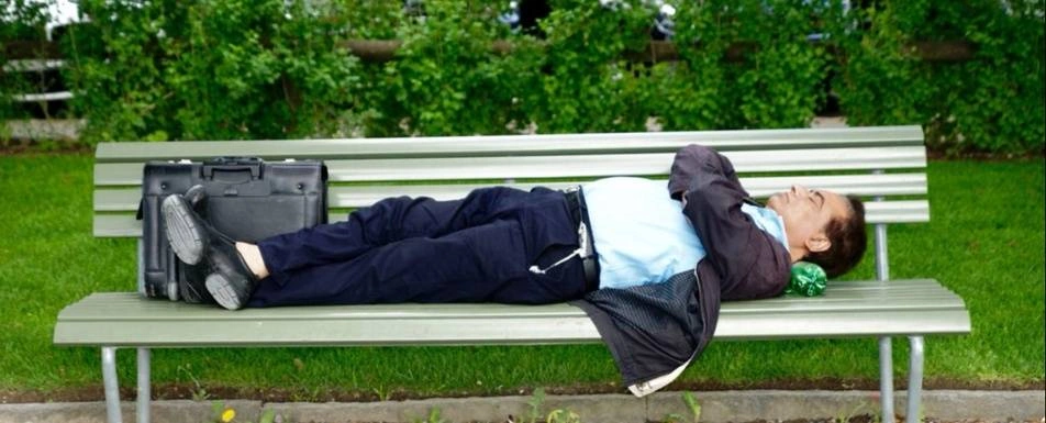 A man lying down on a bench outside.