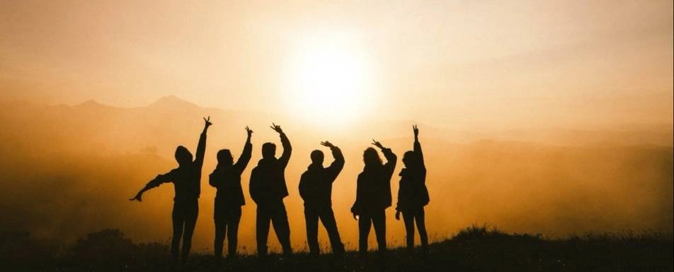 A group of people all holding up peace signs while facing a sunset.