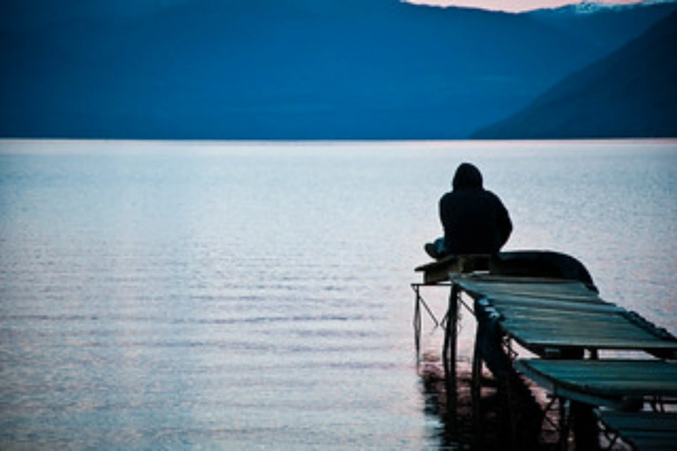Un hombre sentado al borde de un muelle mirando el lago