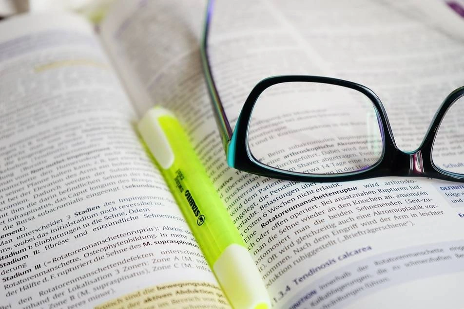 A pair of glasses and a highlighter on an open book.