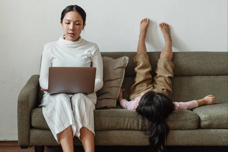 mother working on laptop with child on couch