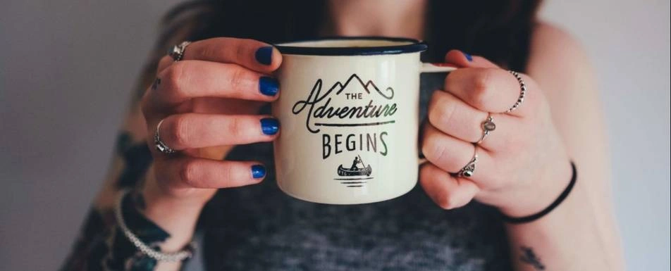 A woman holds a mug that says, "The Adventure Begins."
